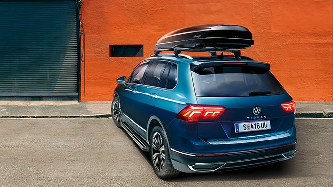 Ein VW Tiguan in blau mit Dachbox parkt vor einem Gebäude